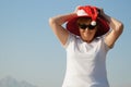 Funny senior woman wearing santa claus hat over sun hat on the sea beach, woman dancing and wishes a merry Christmas and happy new Royalty Free Stock Photo