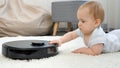 Funny shot of curious little baby boy exploring and looking at working robot vacuum cleaner Royalty Free Stock Photo