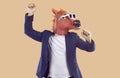 Funny showman in rubber pink horse mask and sunglasses pretends he is singing on beige background. Royalty Free Stock Photo