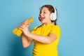 Cute little girl, emotive kid wearing headphones tasting delicious Italian pasta isolated on blue studio background