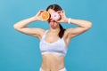 Funny slim woman closing eyes with pink donut and half of juicy grapefruit, having fun showing tongue, choosing between healthy