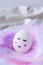 Funny smiley painted egg face in bird feather. Easter decorations. Copy space for text. Pastel colors. Easter greeting card Royalty Free Stock Photo