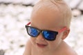 Funny smiling baby boy in sunglasses on the beach. Stones are reflected in the glasses. Little boss on vacation