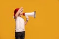 Funny smiling little child boy in Santa hat holding megaphone in hand , smiling and screaming posing on studio background