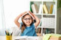 Funny smiling little girl with glasses and a book on her head sitting at table Royalty Free Stock Photo
