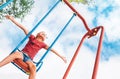 Funny smiling little girl swinging on the swing wide opened an arms with blue sky background Royalty Free Stock Photo