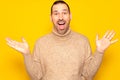 Funny smiling man in beige sweater showing palms up, unexpected surprise gesture isolated over yellow background Royalty Free Stock Photo