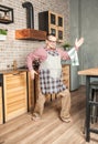 Funny smiling man wearing pinafore with towel dancing on the kitchen