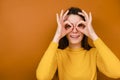 Funny smiling young woman having fun making glasses shape with hands, does funny face with eyes wide open Royalty Free Stock Photo