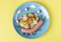 Funny snail from sausage with cucumber and radishes salad on a plate top view - food idea for kids