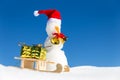 Funny snowman and a sledge with presents in the snow