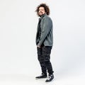 Funny stylish curly guy with a beard dressed in a black t-shirt, gray jacket, khaki pants and sneakers poses in the Royalty Free Stock Photo