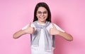 Cute fashionable emotional girl with glasses in a basic T-shirt on a pink background