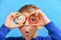 A funny and surprised boy holds a compass in one hand near his eyes and glasses in the other