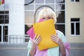 Funny teenage girl outside holding student hides face behind folders