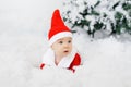 Funny toddler baby in a little Santa Claus costume lies on his stomach on the artificial snow and is surprised Royalty Free Stock Photo