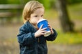 Funny toddler boy having hot chocolate outdoors on sunny autumn day. Child exploring nature. Kid playing in a city park Royalty Free Stock Photo
