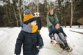 Funny toddler boy and his big sisters having fun with a sleigh in beautiful winter park. Cute child playing in a snow Royalty Free Stock Photo