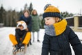 Funny toddler boy and his big sisters having fun with a sleigh in beautiful winter park. Cute child playing in a snow Royalty Free Stock Photo