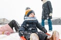 Funny toddler boy and his big sisters having fun with a sleigh in beautiful winter park. Cute child playing in a snow Royalty Free Stock Photo