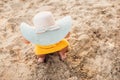 Funny toddler girl in big straw hat sitting barefoot on the sand. Summer vacation Royalty Free Stock Photo