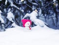 toy snowman in a bright pink cap sitting in the Park with a gift under the tree in glowing garlands Royalty Free Stock Photo