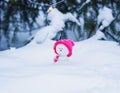 Funny snowman in a bright pink cap sitting in the Park with a gift under the tree in glowing garlands Royalty Free Stock Photo