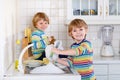 Funny twin boys helping in kitchen with washing dishes