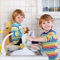 Funny twin boys helping in kitchen with washing dishes