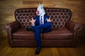 Funny unicorn in elegant suit sits on sofa like a boss and showing rock gesture