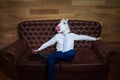 Funny unicorn in suit sits on sofa like a boss. Unusual man resting at home