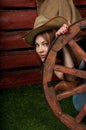Funny Western girl in cowboy hat sitting with wagon wooden wheel. Royalty Free Stock Photo