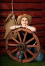 Funny Western girl in cowboy hat sitting with wagon wooden wheel. Royalty Free Stock Photo