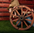 Funny Western girl in cowboy hat sitting with wagon wooden wheel.