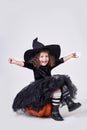 Funny witch girl in a hat sitting on a pumpkin