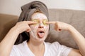 Funny woman with casual clothes, towel on head and beauty mask on face sitting on couch and resting. Relax after taking