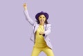 Happy funny young woman in hat and glasses dancing against lilac studio background Royalty Free Stock Photo