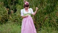 Funny woman in dirndl - traditional festival dress dancing comic on apple garden background. Dance, tomfoolery, positive