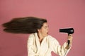 Funny woman drying her long hair with electric fan on a pink background Royalty Free Stock Photo