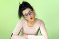 A funny woman with glasses makes stupid faces on a green background. Royalty Free Stock Photo