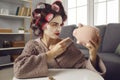 Funny woman in hair curlers shaking finger at piggy bank determined to save up money