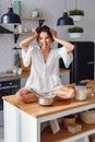 A funny woman with hair curling dressed in white bathrobe feels panic in the kitchen while cooking.