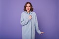 Funny woman with wavy hair standing in studio in blue coat. Wonderful caucasian girl with bright ma Royalty Free Stock Photo