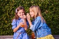 Funny 10-year-old girls of different races are sitting on a Park bench, holding juice bottles in their hands and laughing, sharing