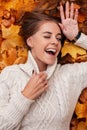 Funny young beautiful woman in a stylish knitted white sweater lies and laughs in the park on orange maple leaves. Attractive Royalty Free Stock Photo