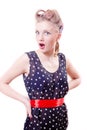 Funny young blond pinup woman in polka dot dress with curlers wonderingly akimbo looking at camera on white