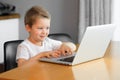 Funny young boy using a laptop computer sitting on top of a table at home Royalty Free Stock Photo