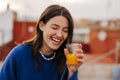 Funny young caucasian woman laughs with her eyes closed, holds glass of juice on blurred background. Royalty Free Stock Photo