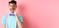 Funny young man in bow-tie look through magnifying glass and showing tongue, smiling happy, having fun on pink Royalty Free Stock Photo