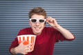 Funny young man in 3D glasses and a popcorn cup looks at the camera and smiles at the dark background Royalty Free Stock Photo